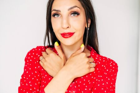 Close-up portrait of glamorous brunette girl with a red lips and fresh make-up, she holding hands with bright manicure near faceの写真素材