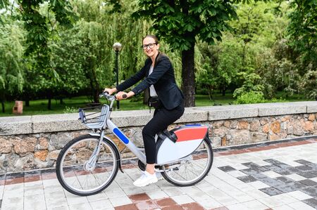 Contemporary businesswoman is riding for work on a bicycle. Young woman in smart casual wear riding bike in the cityの写真素材