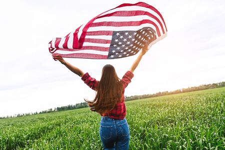Waving in the wind an American flag in the hands of a young girl running on a green captive field, the back view. Independence dayの写真素材