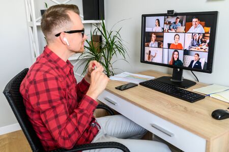 Morning meeting online. Young man connects via video call with coworkers. App for video chat with employeesの写真素材