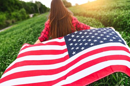Waving in the wind an American flag in the hands of a young girl running on a green captive field, the back view. Independence dayの写真素材