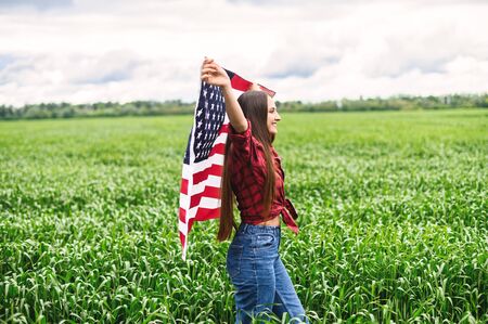 Carefree pretty girl running and smiling on the green field with a blowing flag of USA.の写真素材