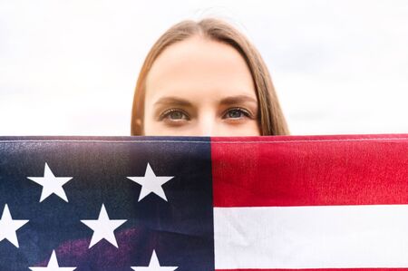 Half face of attractive woman is covered of American flag, like a face mask. Woman looks at camera...