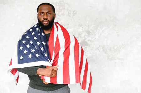 Upset black guy wrapped himself in the flag of America and looks sad at the cameraの写真素材