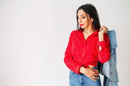 Charming slim girl with jeans and a red shirt posing on a white background, she threw her jacket over her shoulder.の写真素材