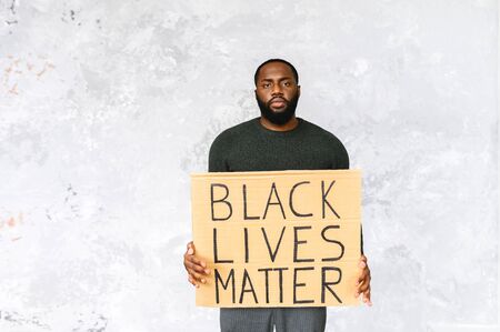 Handsome African-American guy stands with a serious face with a board with inscription black lives matter. Studio shotの写真素材