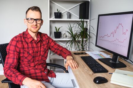 Smiling confident handsome guy wearing glasses using PC for work in the office, he sits at the desk...