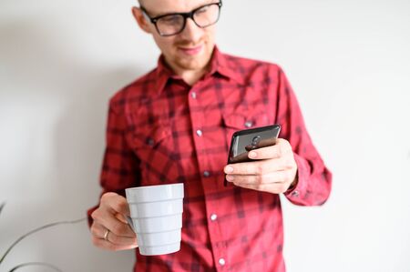 Close-up view of a guy in hipsterish casual plaid shirt having coffee and checking his feed on the...