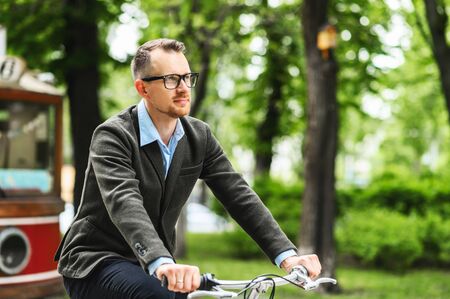 Attractive guy gets to office on a bicycle. Young man in stylish smart casual clothes rides on a...