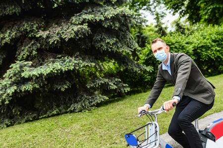 A guy in a medical mask chooses to ride a bicycle to get at the office to avoid crowding in public transport during a pandemic, an epidemicの写真素材