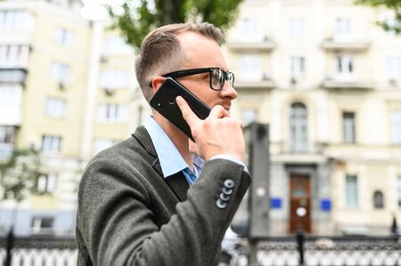 Contemporary businessman wearing trendy eyeglasses and smart casual wear is talking on the smartphone with a business partners outdoorsの写真素材