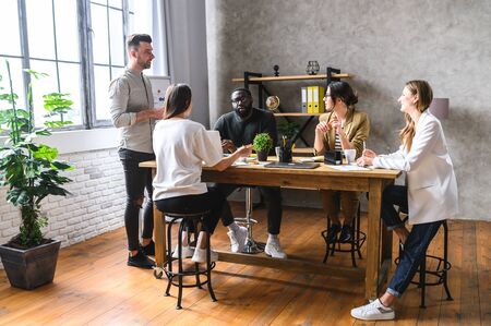 Successful young multiracial team in a modern office. Group of young smart people discuss development strategy of company while sitting at the tableの写真素材