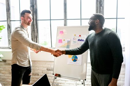 Two businessmen are making a deal, they are shaking their hands. Multiracial coworking, friendly atmosphereの写真素材
