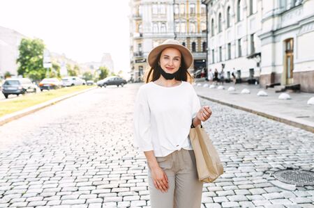 Wear a protective mask in the city. Young happy girl walks around the city with a medical mask lowered on the chinの写真素材
