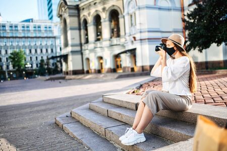 Young woman tourist sightseeing. Girl with a medical mask on her face takes a photo while sitting in the city centerの写真素材