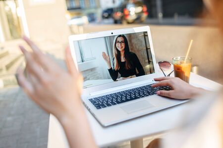 Video call. Webcam shot young woman on the laptop screen, two friends have video chat in summer cafe outdoorsの写真素材