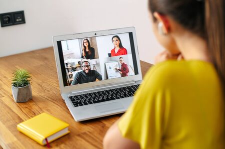 Virtual conference, online meeting. Young woman uses laptop app for communicating with several people friends or employees at same time together. Back view. Video call conceptの写真素材