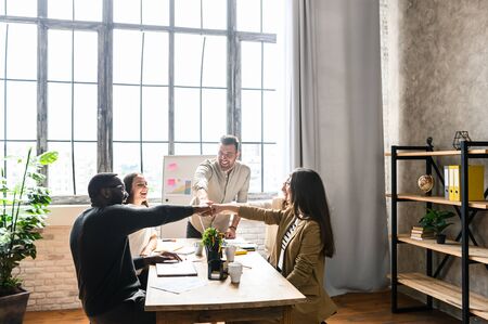 Creative and cheerful multiracial team at the office laughing and they stack their fist together as a sing of concent and team work, a long shotの写真素材