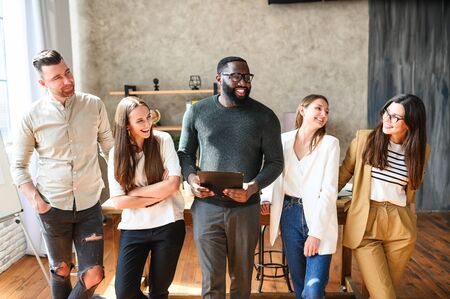 Cohesive cheerful multiracial team in office. They stand in informal relaxed poses, smiling and laughing, they look on each otherの写真素材