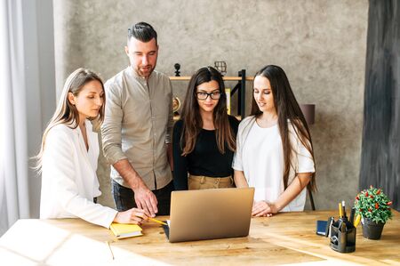 Young serious team of creative people are studing data on the screen of a laptop. They are standing in cosy office and thinking over an information givenの写真素材