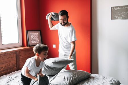 Father spends time with his son. Dad and little son had a pillow fight, they are having fun and laughing on the bed in the cozy bedroomの写真素材