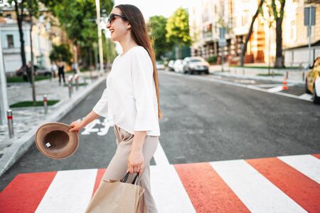 Walk around the city. Beautiful young woman is walking on a pedestrian crossing with a paper shopping bag and laughing. Side viewの写真素材
