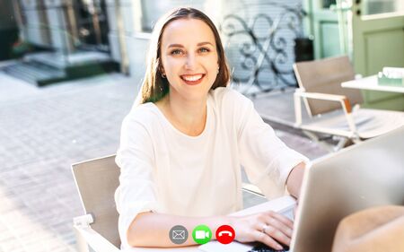 Video call, virtual meeting. Young woman is talking online while sits outdoors in the summer cafeの写真素材