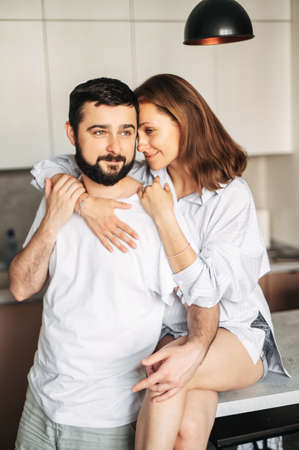 Cozy morning at home. Couple in love hug in the kitchen. A young woman and man in homewear cuddle tenderly indoor. Vertical shotの写真素材