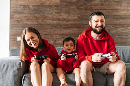 Young family enjoy spending time with play station. Father, mother and son sit on the cozy sofa in living room with a joysticks in hands. Photo with grainの写真素材