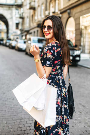 Sales in the stores. Pretty young brunette woman wearing sunglasses looks back with a paper shopping bags in her hand, she had successful shopping dayの写真素材