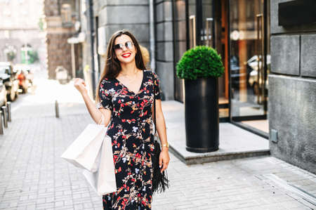 Happy beautiful girl walking on the street with a shopping bags, she satisfied and looks at camera cheerfullyの写真素材
