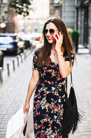 Beautiful brunette woman is walking on the street. Girl flirty talks on the phone and smilesの写真素材