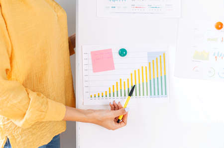 A graph with some raising statistics datas hangs on flip chart, a female hand with a pencil points on itの写真素材