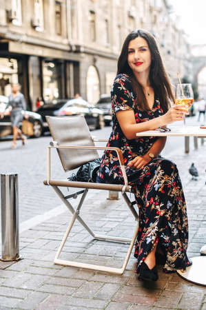 Charming young woman in a dress sits in the summer cafe and going to drink cold cocktailの写真素材