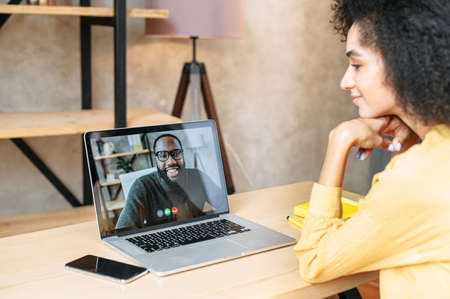 Side view of biracial girl talks via video call with an african-american male colleague or friend on laptop screen. Video call conceptの写真素材