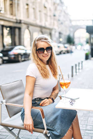 Refresh drink in the hot summer day. Young pretty blonde woman in sunglasses drinks cocktail in the summer cafeの写真素材