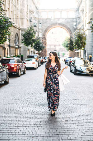 Full length young attractive woman in a long summer dress is walking down the street with a paper shopping bags in handsの写真素材
