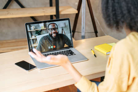 Back view of biracial girl talks via video call with an african-american male colleague or friend on laptop screen. Video call conceptの写真素材