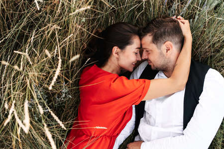 Top view of couple in love lays and hugs in tall grass in the meadow, they touch their noses