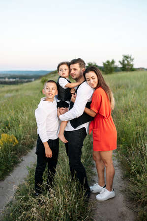 Happy family outdoors. Young mom and dad with two sons stand in a field by the countrysideの写真素材