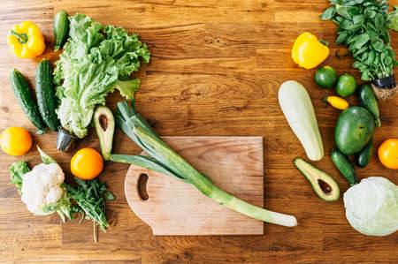 Salad preparation. Top view a leek on a wooden kitchen board surrounded various fresh vegetables. Vegetarian food concept. Copy-space, mockupの写真素材