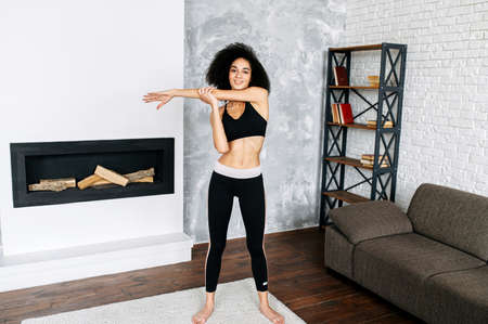 A young athletic mixed-race girl in sportswear does stretching before workout, she is warming out upper body. Healthy lifestyle conceptの写真素材