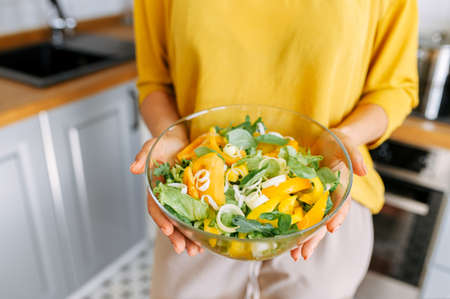 A glassy bowl with diet salad in female hands indoorの写真素材
