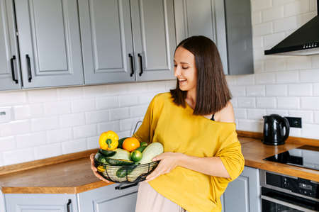 Vegetarian lifestyle. A young, healthy woman looks at a basket full of fresh farm vegetables in her handsの写真素材