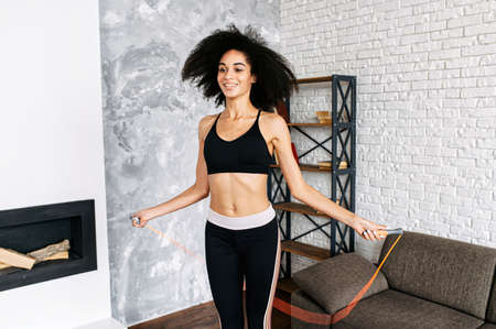 An attractive young African-American woman is jumping rope at home. Healthy lifestyle concept.の写真素材
