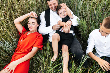 Happy young family of four have a fun outdoors. Mother, father and two sons lay on the grass in the meadowの写真素材