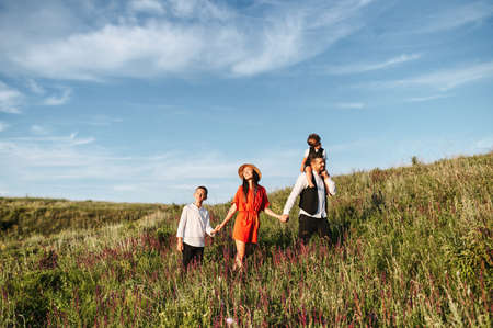 Happy loving family walking on field with flowers. They are holing each other by the hand. A young...