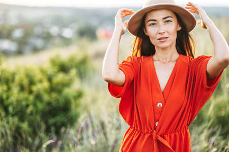 Charming girl in hat posing in the countryside. Woman in red looks at camera with a passionの写真素材