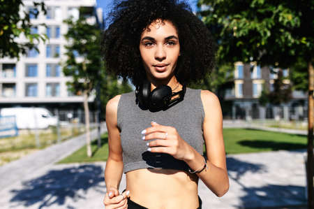 Charming African-American young woman is jogging outdoors. A girl with an afro hairstyle in short...