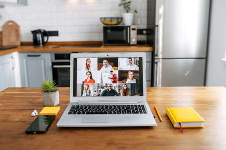 App for video meeting. Laptop on the table in cozy kitchen room, video call with group of people on the screen. No people in the roomの写真素材
